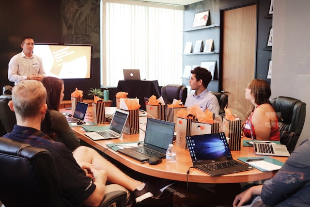 Man standing in front of people sitting beside table with laptop computers